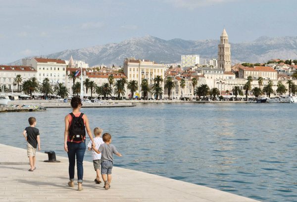 A family walks along the shore in Split, Croatia, with old buildings in the background.